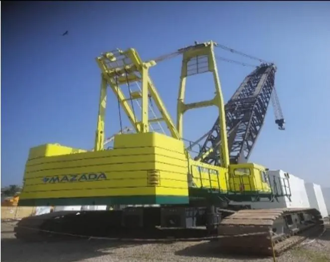 A large yellow Mazada crawler crane with its lattice boom laid down on a project site.