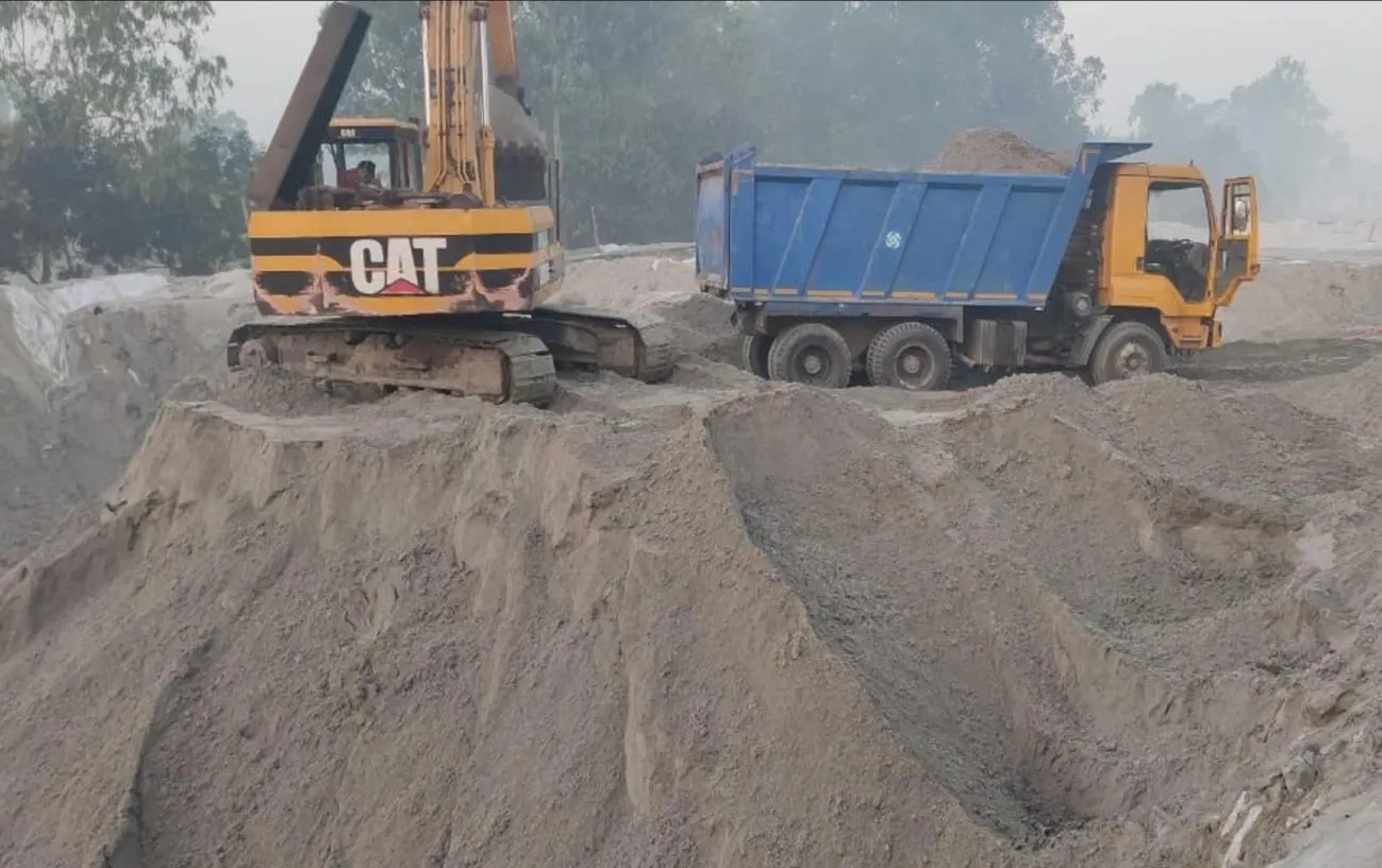 A CAT excavator loading sand into a tipper truck on a large fill site.
