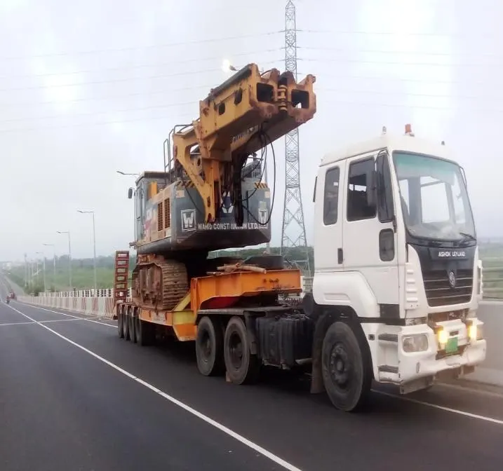 A low-bed trailer carrying a tracked drilling rig along a Bangladeshi highway.