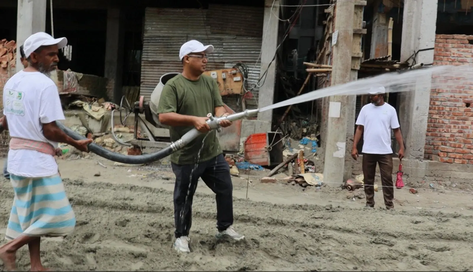 Three S&T Enterprise crew members in branded caps and shirts working a hose to spray SoilBinder solution onto a prepared road base.