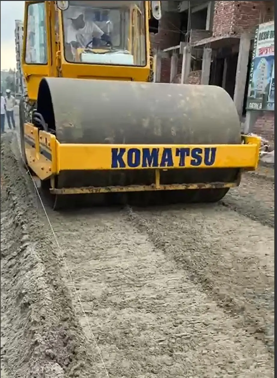A Komatsu vibratory soil compactor rolling a freshly mixed SoilBinder road base between apartment blocks.